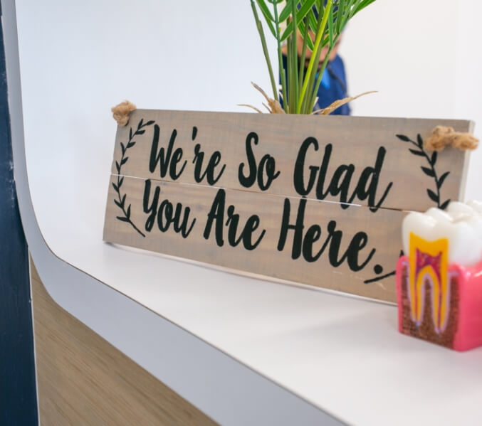Sign reading we're so glad you're here in dental office reception area
