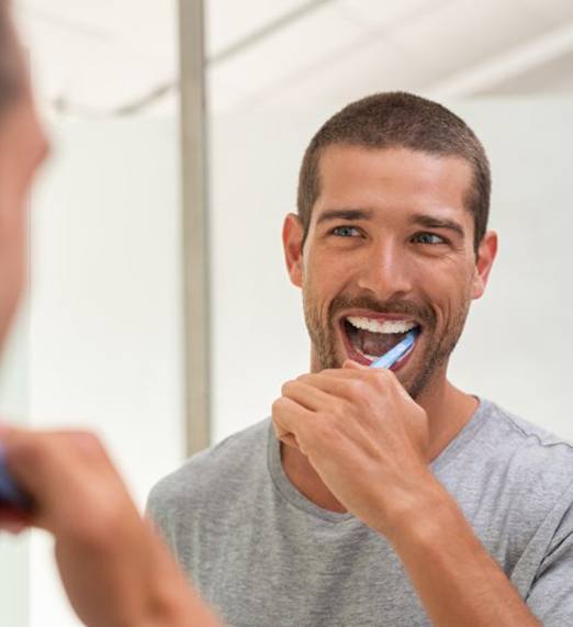 man brushing teeth in bathroom mirror 